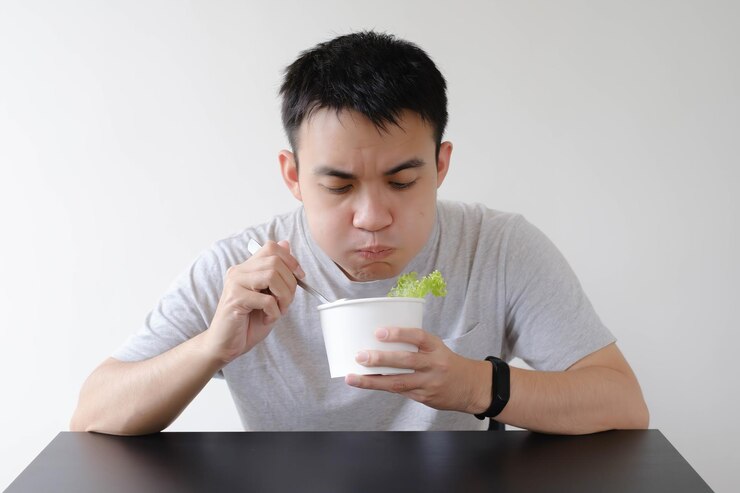Un joven asiático está comiendo comida en un tazón de papel blanco desechable con la boca masticada