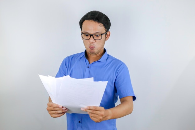 El joven asiático está enojado y enojado cuando mira un documento en papel Hombre indonesio con camisa azul