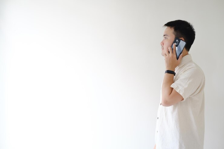El joven asiático está hablando por teléfono mientras mira a su lado derecho o izquierdo de la cámara