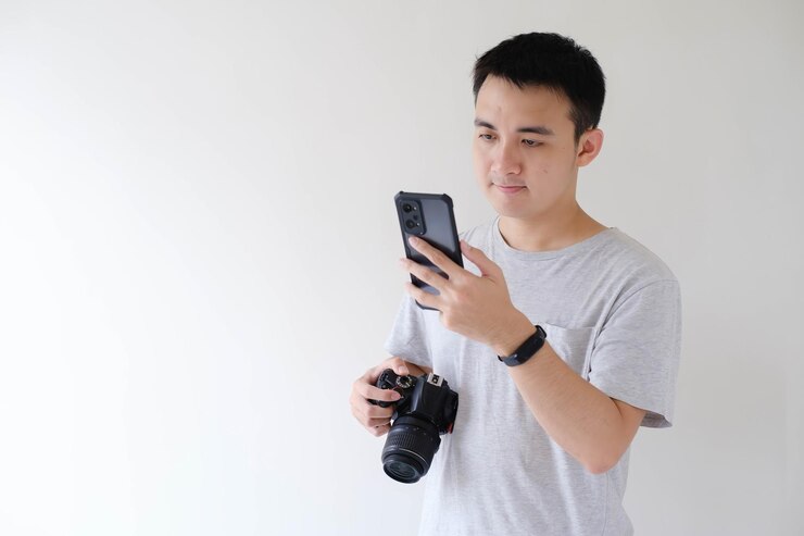 Un joven asiático está mirando un teléfono inteligente y sosteniendo una cámara DSLR