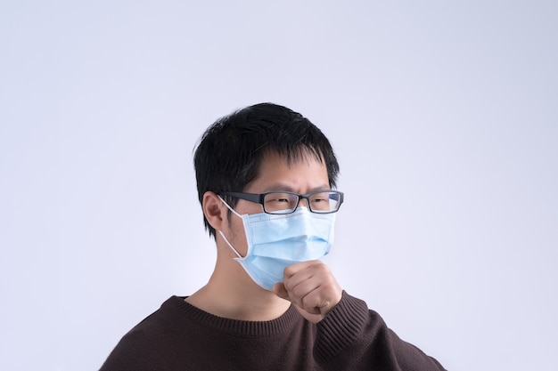 El joven asiático está tosiendo, sintiéndose mal, vomitando enfermo con el uso de una mascarilla médica azul aislada sobre fondo blanco, de cerca, copie el espacio.