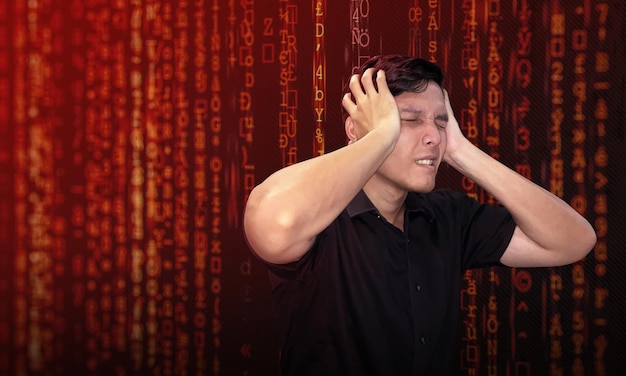 Joven asiático estresado debido a la sobrecarga de información código binario rojo en el fondo