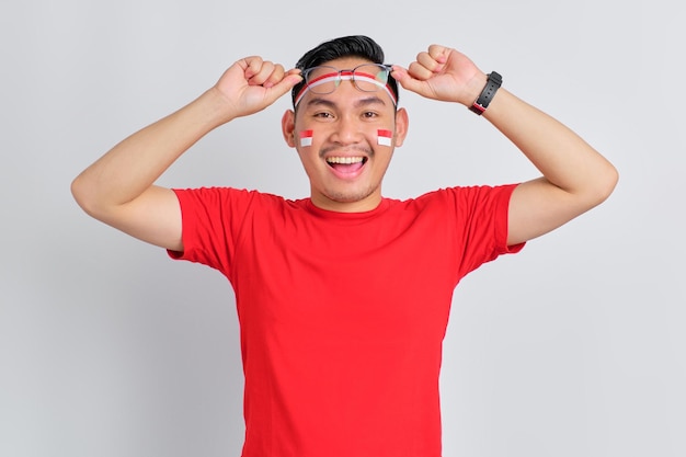 Un joven asiático feliz celebrando el día de la independencia de Indonesia se quita las gafas aisladas de fondo blanco