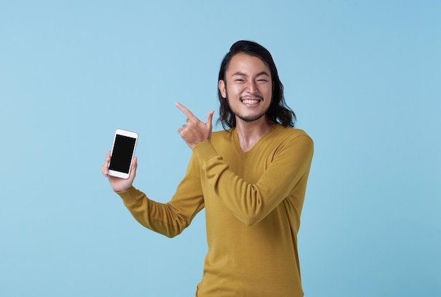 Un joven asiático feliz y complacido que muestra un teléfono inteligente en la pantalla y señala el espacio de la copia