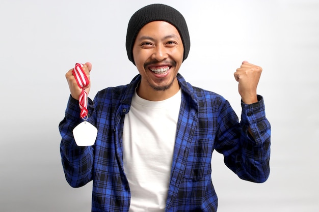 Un joven asiático feliz levanta un puño cerrado en celebración mientras sostiene con orgullo una medalla