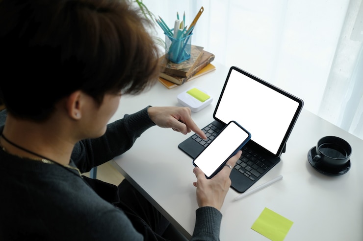 Foto joven asiático independiente sentado en su lugar de trabajo y usando teléfono móvil.