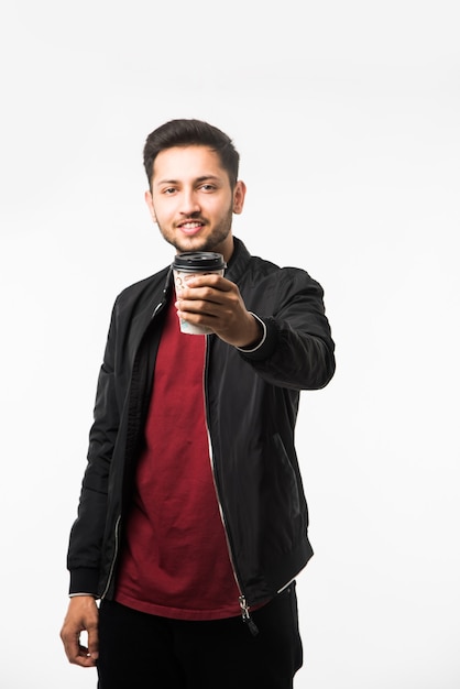 Joven asiático indio sosteniendo una taza de café de papel con una tapa de plástico negra aislada sobre un fondo blanco en el estudio, publicidad de café