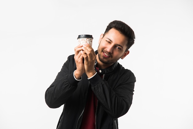 Joven asiático indio sosteniendo una taza de café de papel con una tapa de plástico negra aislada sobre un fondo blanco en el estudio, publicidad de café