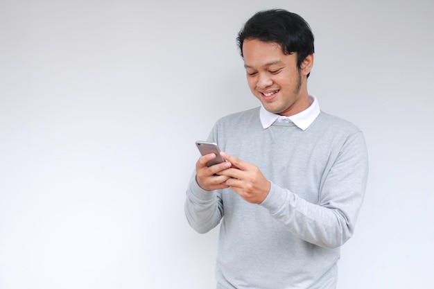 El joven asiático inteligente está feliz y sonriendo cuando usa un teléfono inteligente en el fondo del estudio