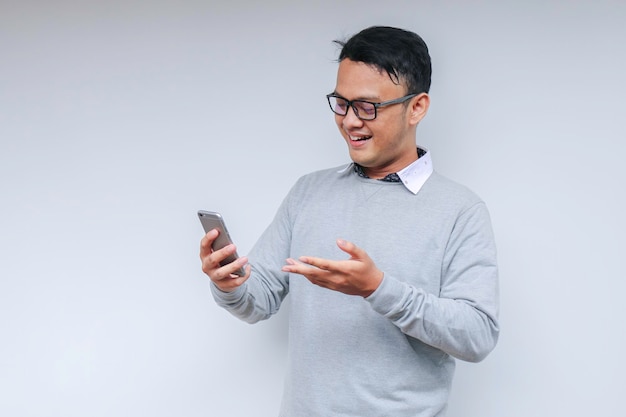 El joven asiático inteligente está feliz y sonriendo cuando usa un teléfono inteligente en el fondo del estudio