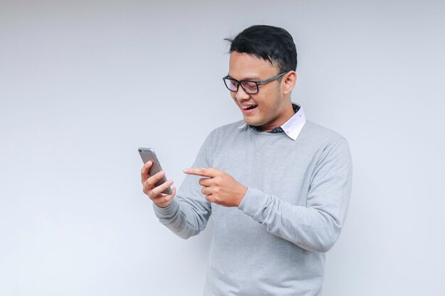 El joven asiático inteligente está feliz y sonriendo cuando usa un teléfono inteligente en el fondo del estudio