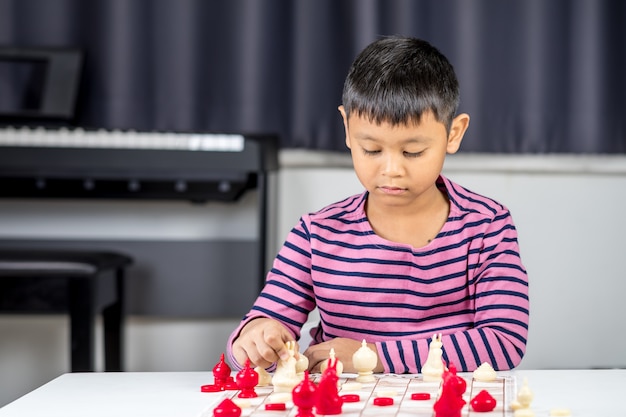 Joven asiático jugando al ajedrez en la habitación