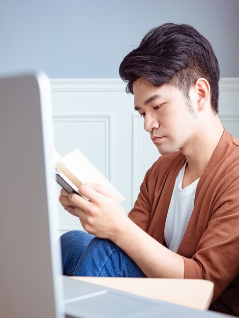 Joven asiático leyendo un libro mientras se relaja en casa