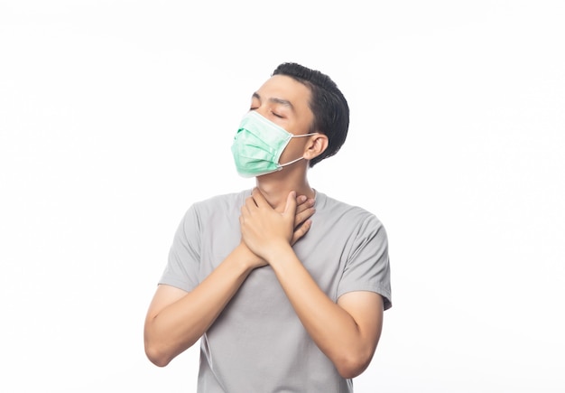 Joven asiático con máscara higiénica que sufre dolor de garganta, 2019-nCoV o coronavirus. Enfermedades respiratorias transmitidas por el aire, como las peleas pm 2.5 y gripe Foto de estudio aislado en la pared blanca