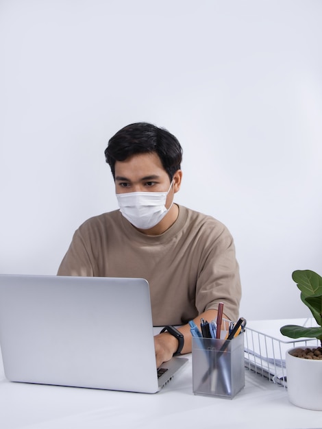 Joven asiático con una máscara protectora, proyecto de trabajo en su computadora portátil en la oficina. tiro del estudio aislado en el fondo blanco.