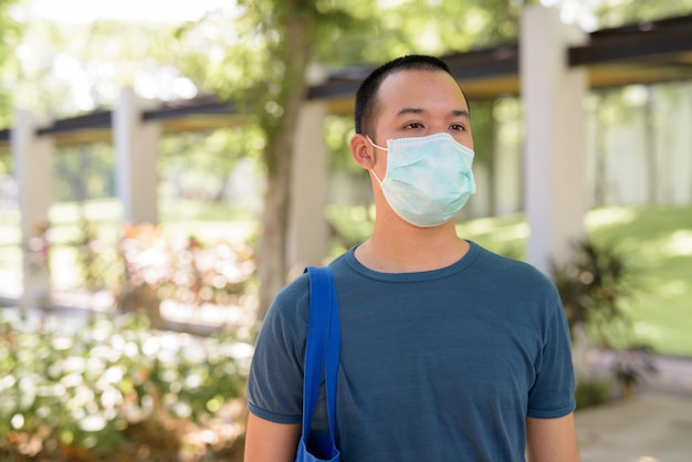 Joven asiático con máscara para protegerse del brote de coronavirus con la naturaleza al aire libre