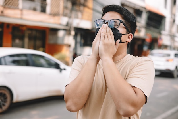 Joven asiático con mascarilla para proteger PM 25 proteger la contaminación contra el smog y los virus en la carretera en la ciudad Concepto de calentamiento global Concepto de salud Concepto de contaminación ambiental