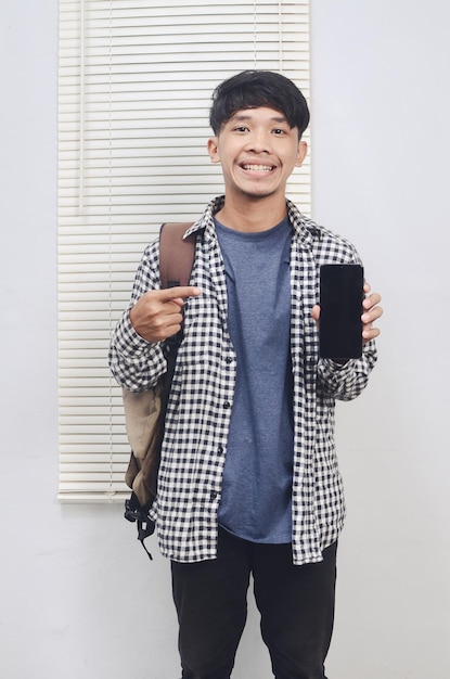 Joven asiático con mochila sonriendo alegremente mostrando la pantalla del teléfono