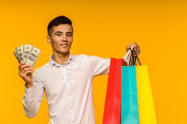 Joven asiático mostrando su bolsa de compras y dinero sobre fondo amarillo