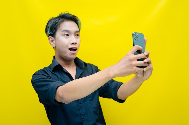 Un joven asiático muy contento con el pelo teñido de peek a boo con una camisa negra sosteniendo un teléfono