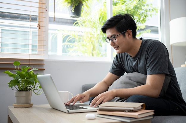 Joven asiático navegando por internet con ordenador portátil en casa.