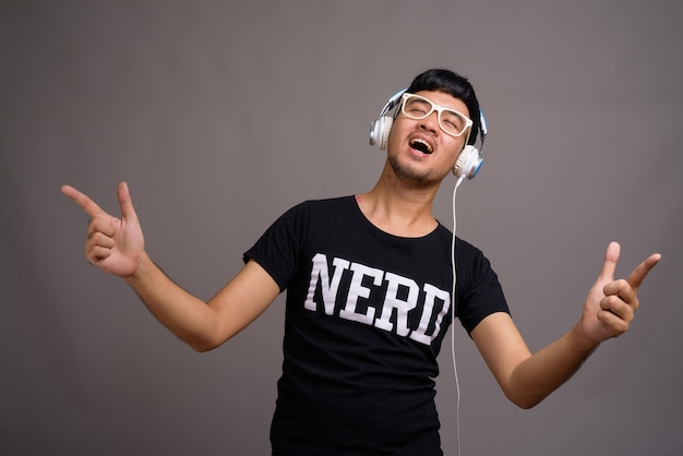 Joven asiático nerd escuchando música contra gris