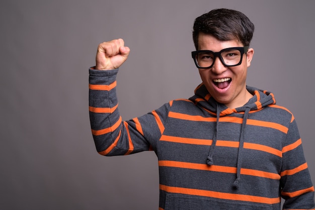 Joven asiático nerd hombre vestido con capucha contra la pared gris