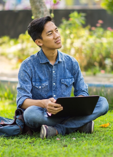Joven asiático pensando en ideas en el parque usando laptop