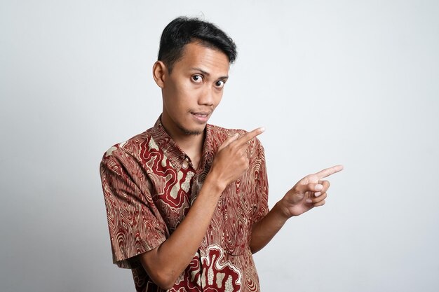 Foto joven asiático con piel bronceada con camisa batik apuntando al espacio vacío lateral para publicidad necesita fondo blanco