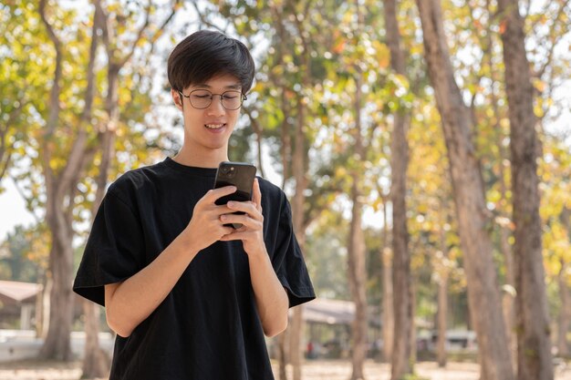 Un joven asiático positivo usando su teléfono inteligente en un parque hablando con sus amigos