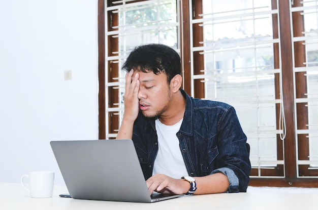 Joven asiático que siente estrés y se confunde cuando trabaja con una laptop en la mesa