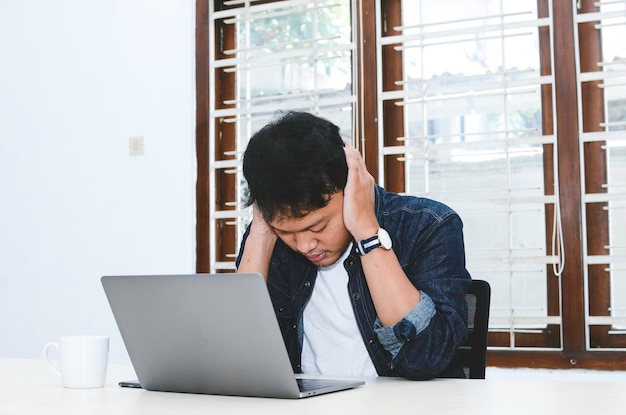 Joven asiático que siente estrés y se confunde cuando trabaja con una laptop en la mesa