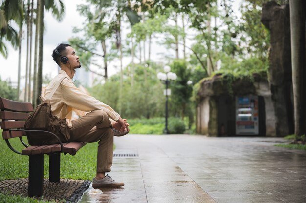 Un joven asiático relajarse y relajarse escuchando música con auriculares en el parque. Buena sensación del día soleado en el jardín en el tiempo libre de vacaciones.