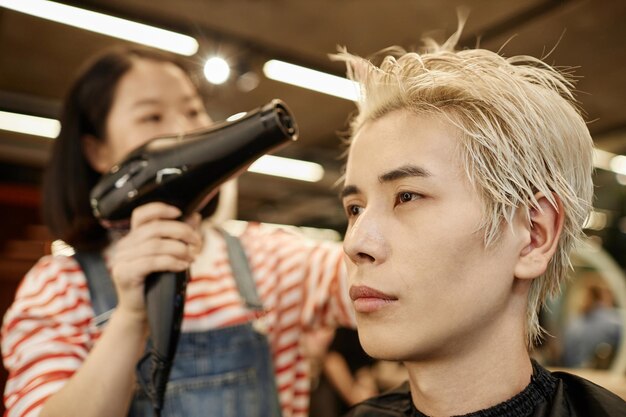 Foto un joven asiático en un salón de belleza con un peluquero secando el cabello.