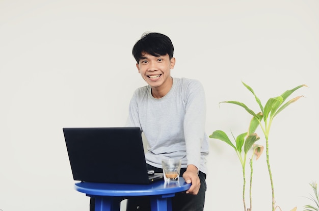 Joven asiático sentado en la computadora portátil con una cara feliz