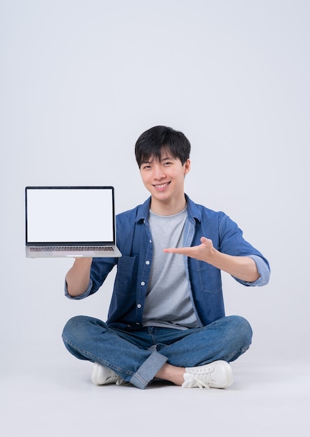 Un joven asiático sentado y usando una laptop con fondo blanco