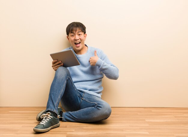 Joven asiático sentado usando su tableta sorprendido, se siente exitoso y próspero