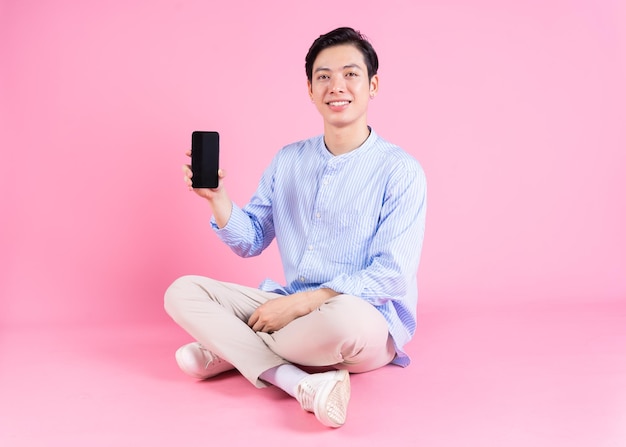 Joven asiático sentado y usando un teléfono inteligente en el fondo