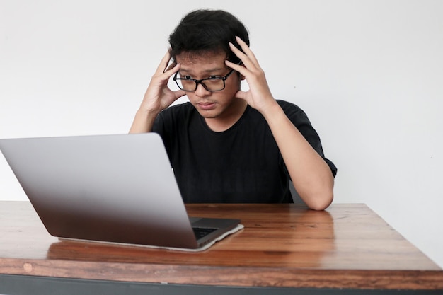 Joven asiático sintiéndose estresado y confundido con el trabajo en una laptop Indonesia El hombre usa camisa negra Fondo gris aislado