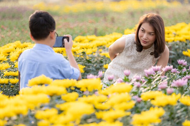 Joven asiático con smartphone para tomar fotos de su madre en el jardín de flores tropicales, concepto para viajes como turismo en el campo de la agricultura.