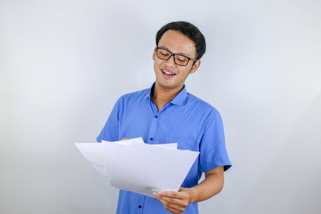 El joven asiático sonríe y es feliz cuando mira un documento en papel Hombre indonesio con camisa azul