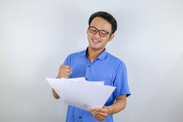 El joven asiático sonríe y es feliz cuando mira un documento en papel Hombre indonesio con camisa azul