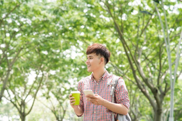 Joven asiático sonriendo y usando el teléfono en el parque