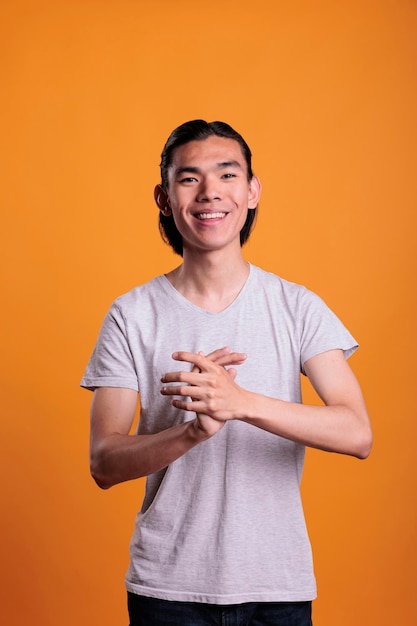 Joven asiático sonriente alegre aplaudiendo, mirando a la cámara. Adolescente de risa positiva con expresión facial alegre aplaudiendo, persona atractiva de pie, retrato de plano medio