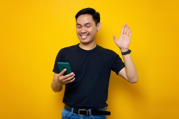 Un joven asiático sonriente con una camiseta informal mirando el teléfono móvil se siente alegre leyendo buenas noticias aisladas en un fondo amarillo Concepto de estilo de vida de la gente