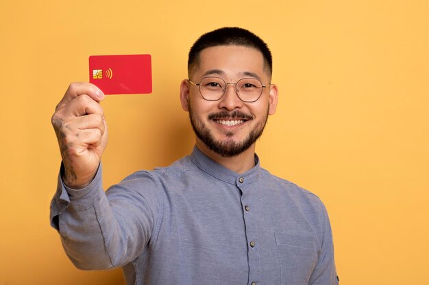 Un joven asiático sonriente mostrando su tarjeta de crédito a la cámara.