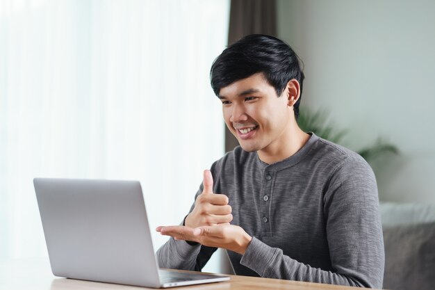 Joven asiático sordo discapacitado usando una computadora portátil para el aprendizaje de llamadas de videoconferencia en línea y la comunicación en lenguaje de señas.