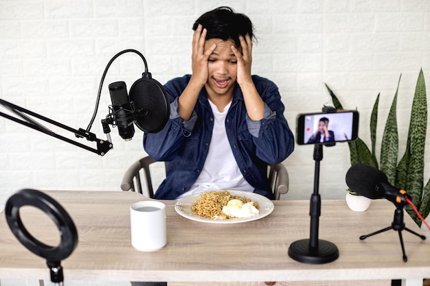 Un joven asiático se sorprendió al ver fideos en el plato durante la grabación de un vlog de comida en un smartphone.