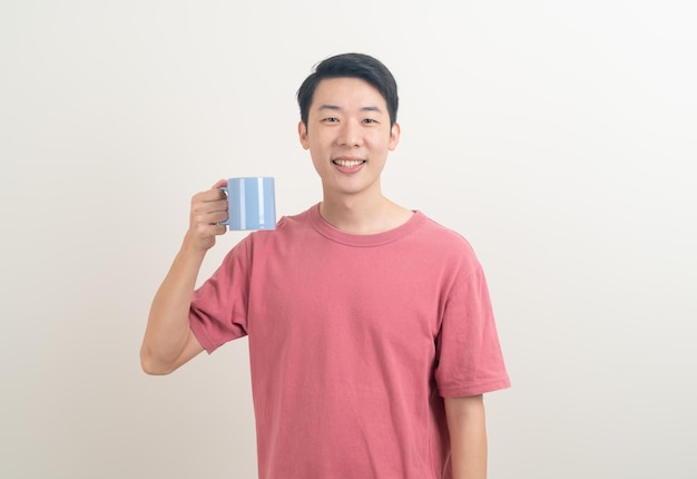 Joven asiático sosteniendo la taza de café con cara sonriente sobre fondo blanco.
