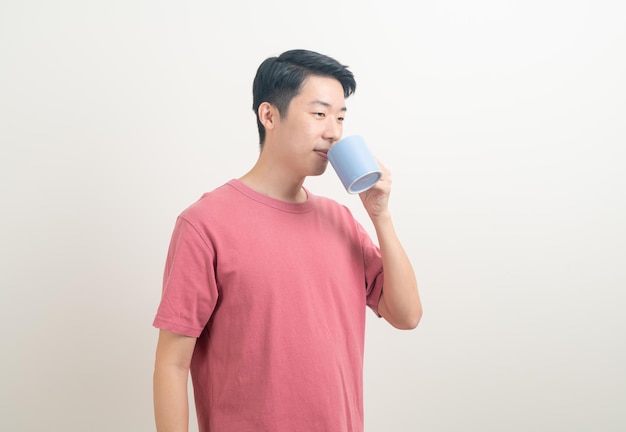 Joven asiático sosteniendo una taza de café con cara sonriente sobre fondo blanco.
